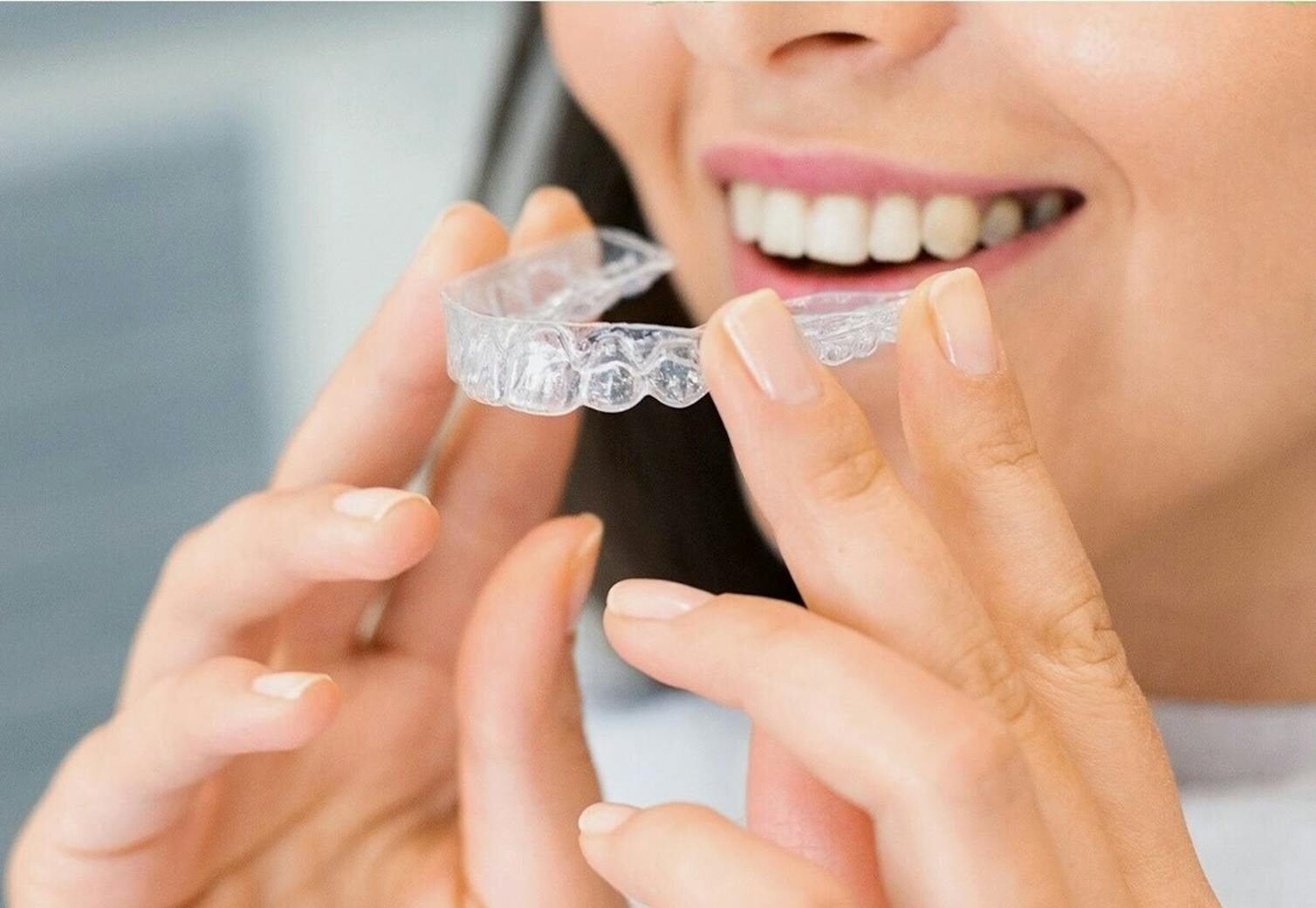 Close-up of a woman holding a clear dental aligner, showcasing dental health and a bright smile.