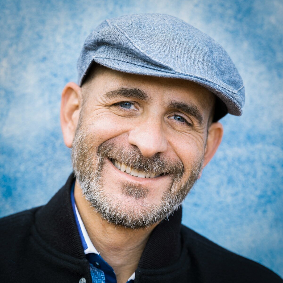 a smiling man wearing a hat and a black jacket